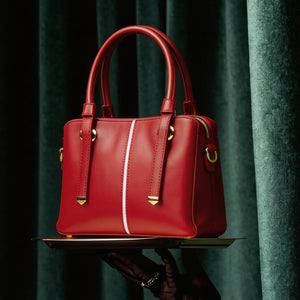 Red handbag held by a gloved hand against a dark curtain background
