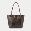 A dark brown crocodile-embossed leather tote bag with matching brown shoulder straps and a small gold logo plaque on the front, set against a solid light gray background.