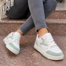 White low-top sneakers with mint green accents worn by a person sitting on stone steps, paired with gray jeans.