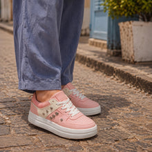 A person wearing pink low-top sneakers with white soles and decorative silver studs, paired with loose blue pants, standing on a cobblestone street.
