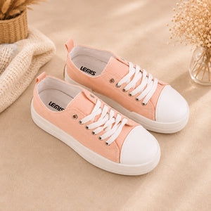 A pair of pastel pink canvas low-top sneakers with white rubber toe caps and white laces, displayed on a beige fabric surface with decorative dried flowers and a woven textile in the background. The brand name 'LEMLIS' is visible on the insole.