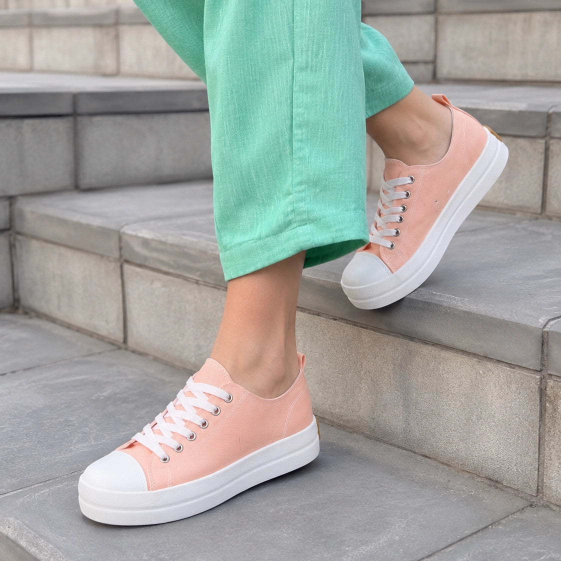 A person wearing mint green pants and light pink low-top platform sneakers with white rubber soles, standing on gray stone steps.