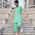 A woman wearing a light green two-piece linen set consisting of a short-sleeve tunic and wide-leg pants, walking down outdoor stone steps.